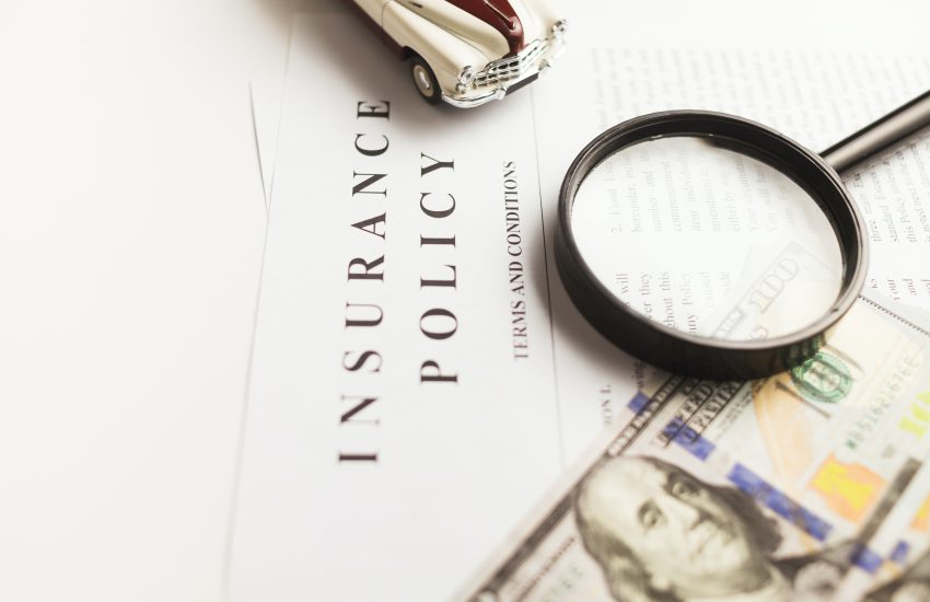insurance policy paperwork on a desk with a dollar bill and a magnifying glass